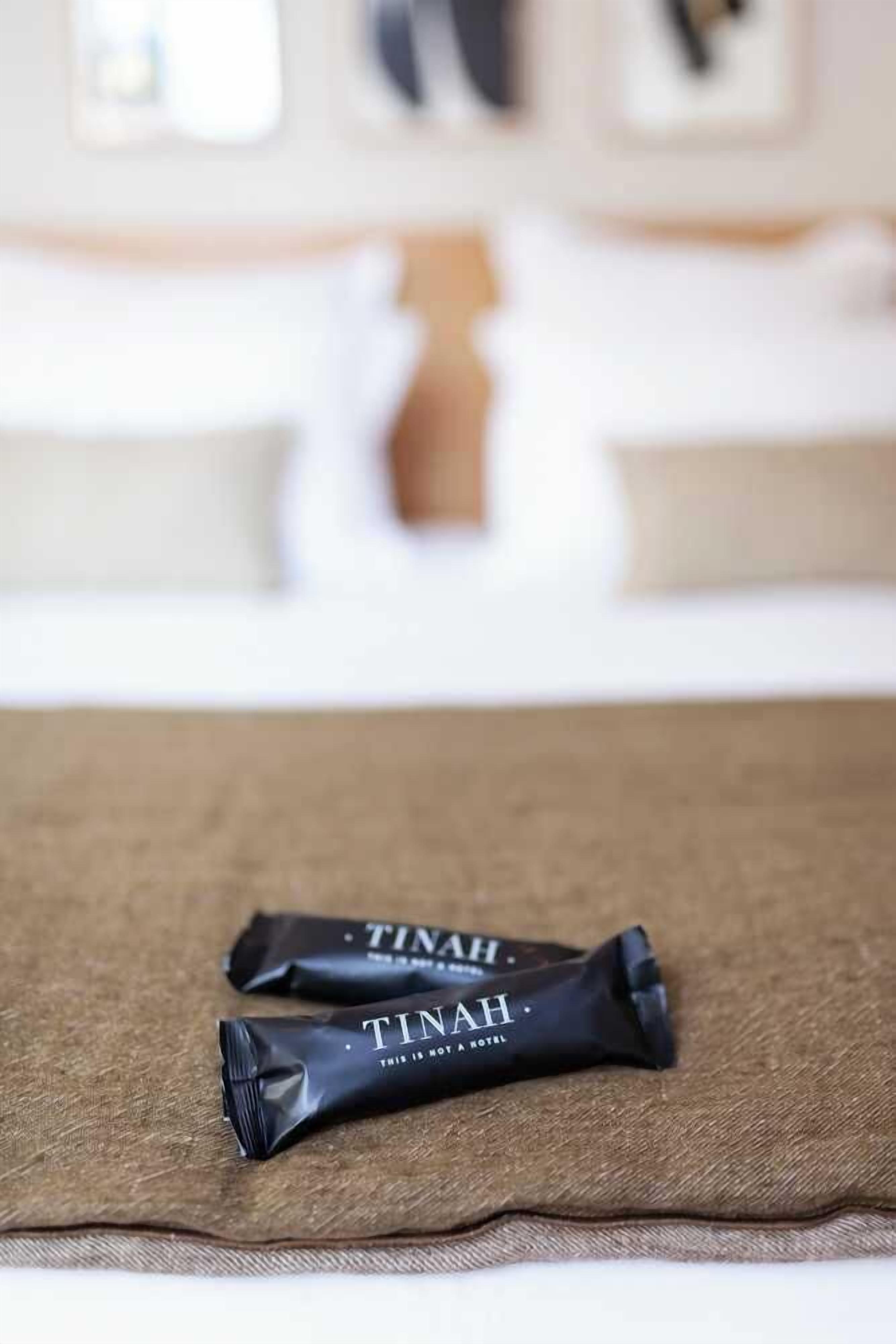 Two black packages labeled "TINAH" on a brown fabric surface in a hotel room.