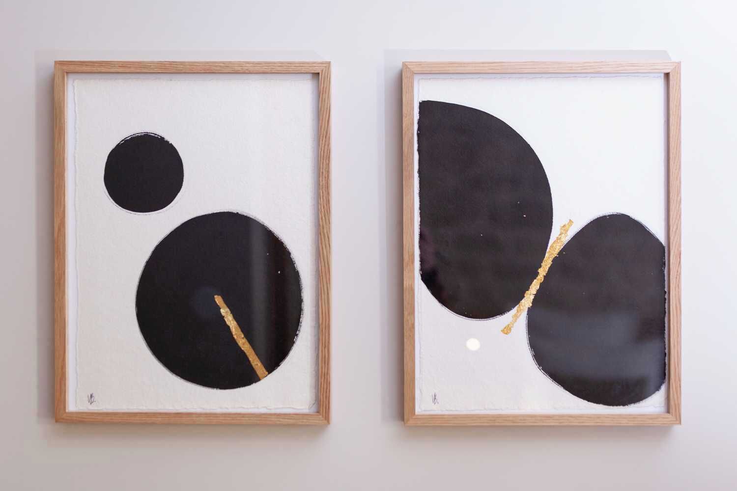 Two framed abstract paintings with wooden frames on a plain wall.