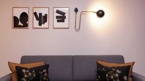 Un canapé gris agrémenté de coussins à motifs floraux, et au-dessus, sur le mur, trois œuvres d’art abstraites encadrées.