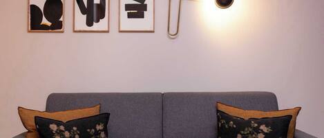 A grey sofa with floral pillows and three framed abstract artworks on the wall above.