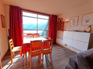 A dining area with a table and chairs, a view of mountains through large windows, and a white cabinet with kitchenware. - Studio Cabin Sleeps 6 - Piau-Engaly (Piau-Engaly)