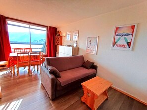 A living room with a sofa, a wooden table, a dining area with a table and chairs, and a large window with a view. - Studio Cabin Sleeps 6 - Piau-Engaly (Piau-Engaly)