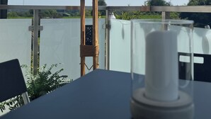 Taula amb portaveles blanc sota una tenda estriada, una cadira de fusta i vista a una tanca i vegetació.