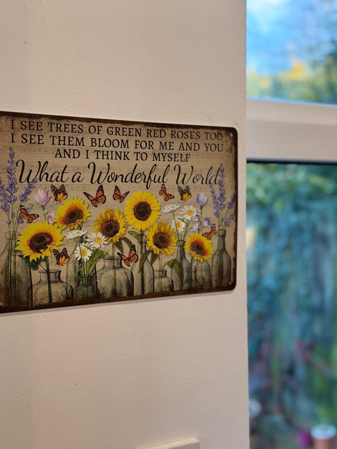 Ein dekoratives Schild mit floralem und Schmetterlingsdesign, das ein Zitat über eine wundervolle Welt zeigt.