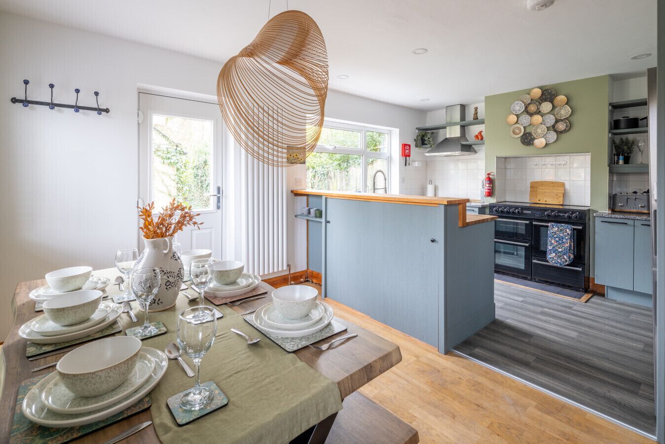 A modern kitchen with a central island, a dining area with a table set for four, and a view of the outdoors through the window.
