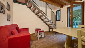 Een kamer met een trap, een rode bank, een kleine tafel en uitzicht door een glazen deur.