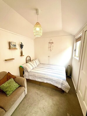 Un dormitorio con cama, sofá, lámpara colgante, atrapasueños en la pared y radiador.