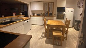 Une cuisine de taille réduite avec une table et des chaises en bois, des placards blancs, un four encastré et une horloge au mur.