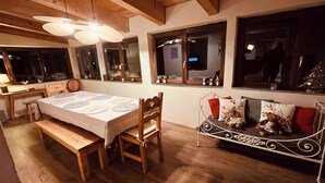 Un coin repas avec une table en bois dressée pour six personnes, un banc et un canapé en métal agrémenté de coussins décoratifs.