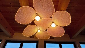 Une pièce avec un plafond en bois et un luminaire fait de fibres tressées. Trois fenêtres offrent une vue sur des montagnes enneigées.