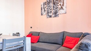 Ett modernt vardagsrum med en grå soffa, röda kuddar, ett matbord med stolar och ett väggmonterat konstverk som föreställer en tiger.
