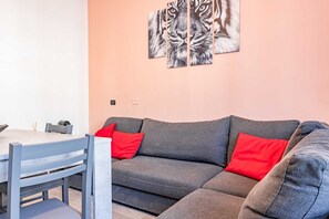 Ein modernes Wohnzimmer mit einem grauen Sofa, roten Kissen, einem Esstisch mit Stühlen und einem Wandbild mit einem Tiger.