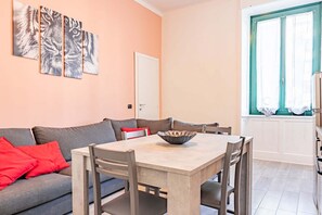 Ein Wohnzimmer mit grauem Sofa, roten Kissen, einem Holzesstisch und einem Fenster mit Vorhängen.
