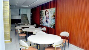 Un salón de conferencias con mesas y sillas redondas, una escalera y un cuadro grande en la pared.