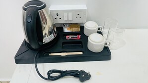 Una cafetera, dos tazas, una caja de cápsulas de café, unos palillos y un cable de alimentación sobre una bandeja negra.
