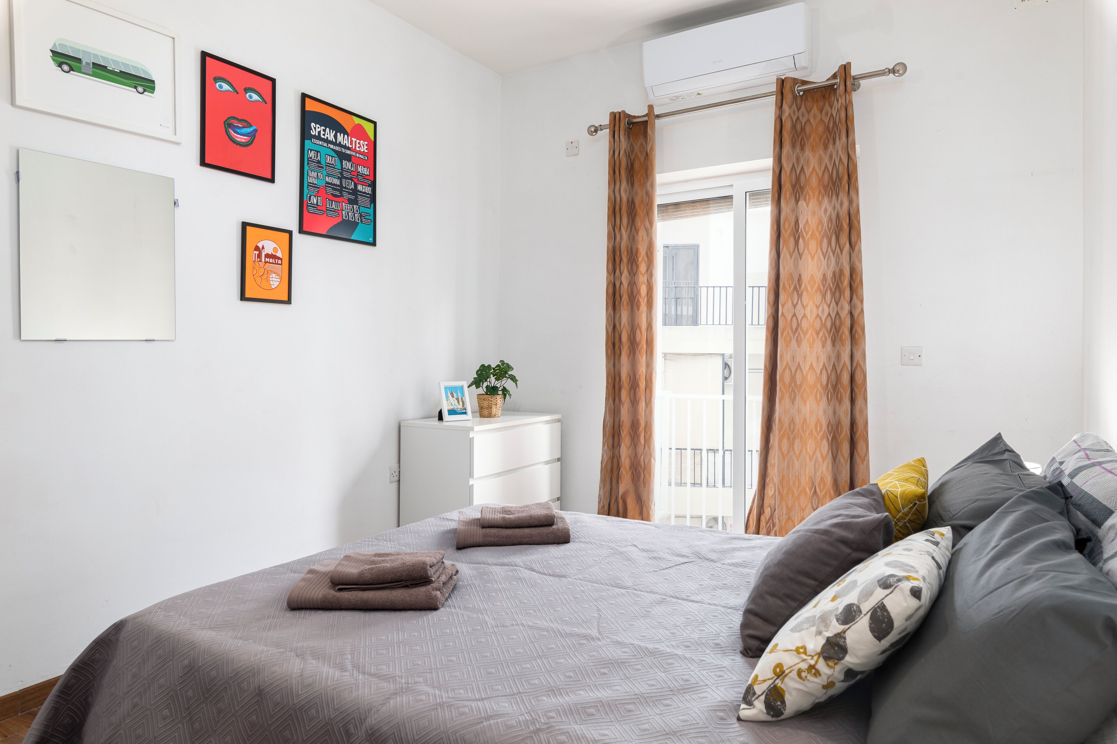 A bedroom with a bed, pillows, a nightstand, a potted plant, and wall art.