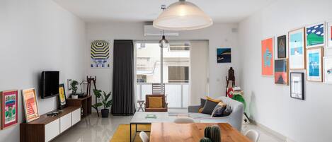 A modern living room with a wooden dining table, a sofa, and a TV on a wooden console.