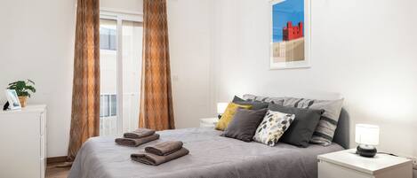 A neatly made bed with a grey patterned bedspread, a bedside lamp, and a framed picture on the wall.