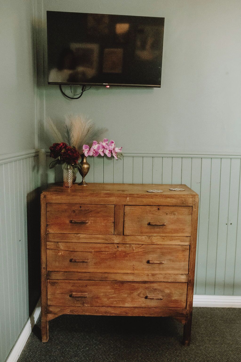 Un aparador de madera con cajones, un florero con flores y un televisor de pantalla plana montado en la pared.