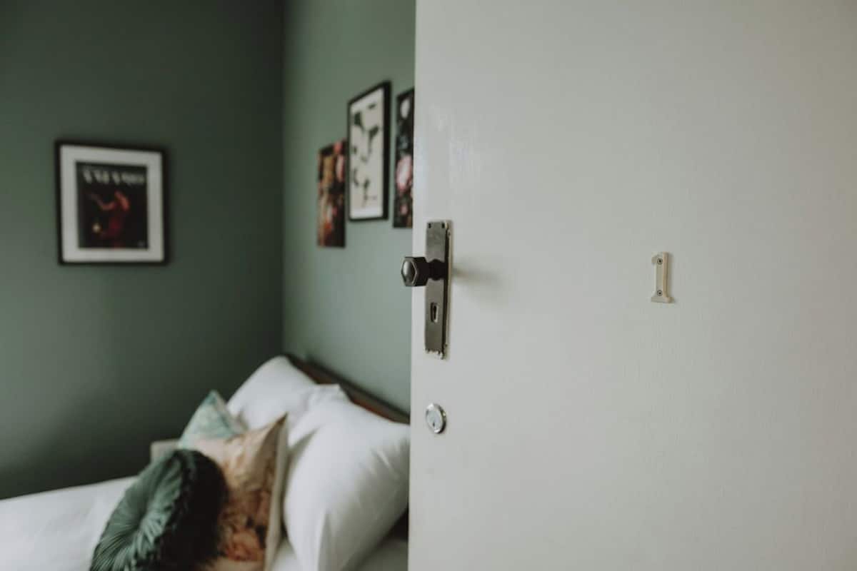 A room with a bed, a door with a lock, and a wall with framed pictures.