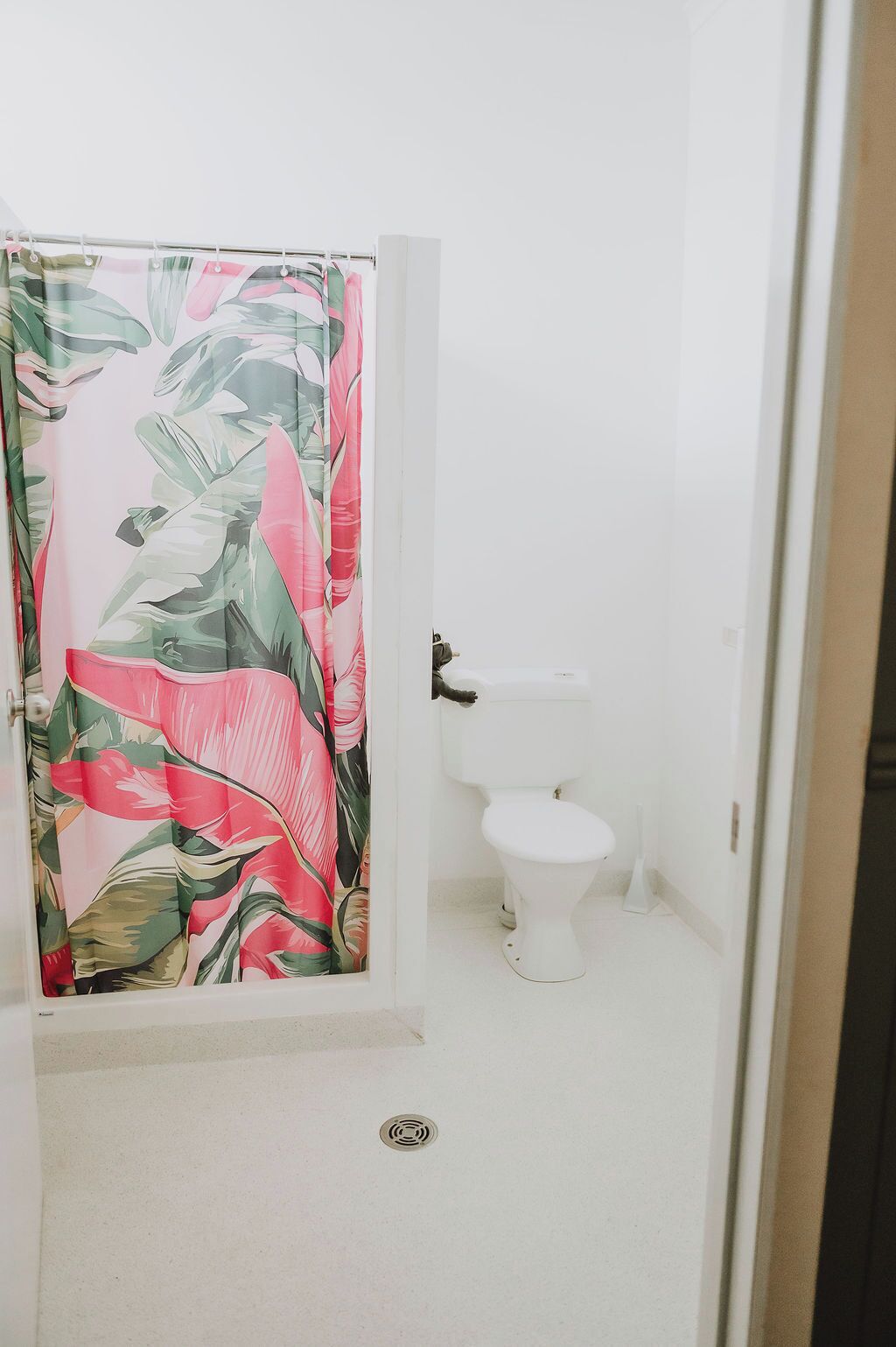 A bathroom with a toilet, a shower curtain with a tropical leaf pattern, and a white sink.