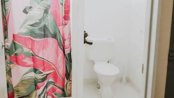 A bathroom with a toilet, a shower curtain with a tropical leaf pattern, and a white sink.
