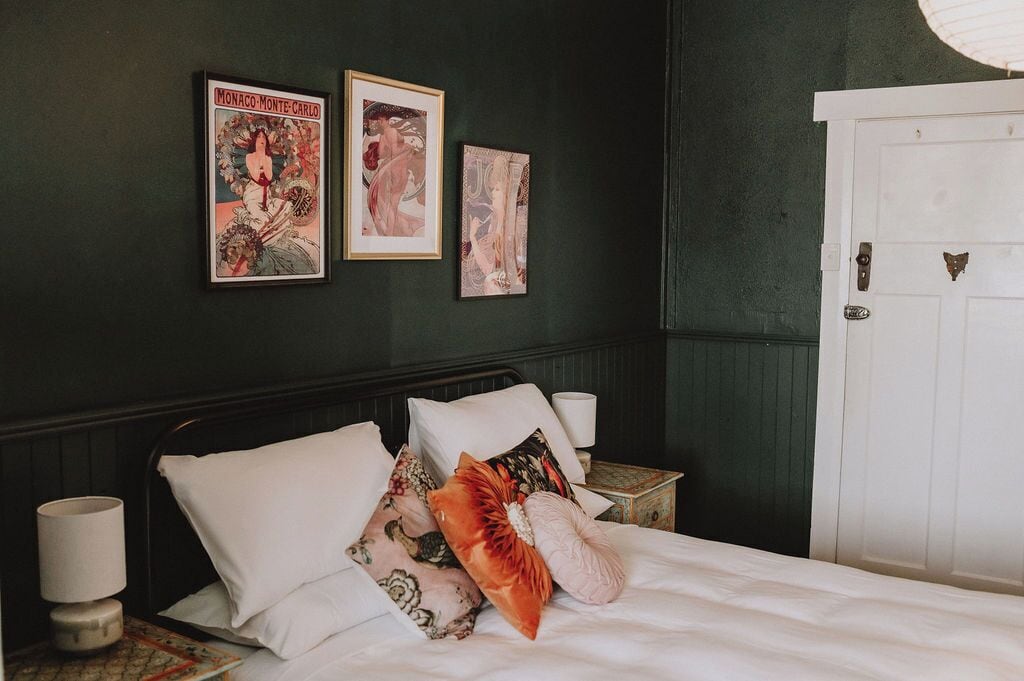 A bedroom with a bed, pillows, a nightstand, a lamp, and two framed posters on the wall.