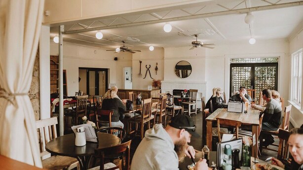 A restaurant with multiple tables and chairs, ceiling fans, and a brick wall. - The Kentish Tasmania (Oatlands)