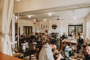 A restaurant with multiple tables and chairs, ceiling fans, and a brick wall.