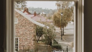 A view through a window of a brick building with a red roof, a street lamp, and trees. - The Kentish Tasmania (Oatlands)