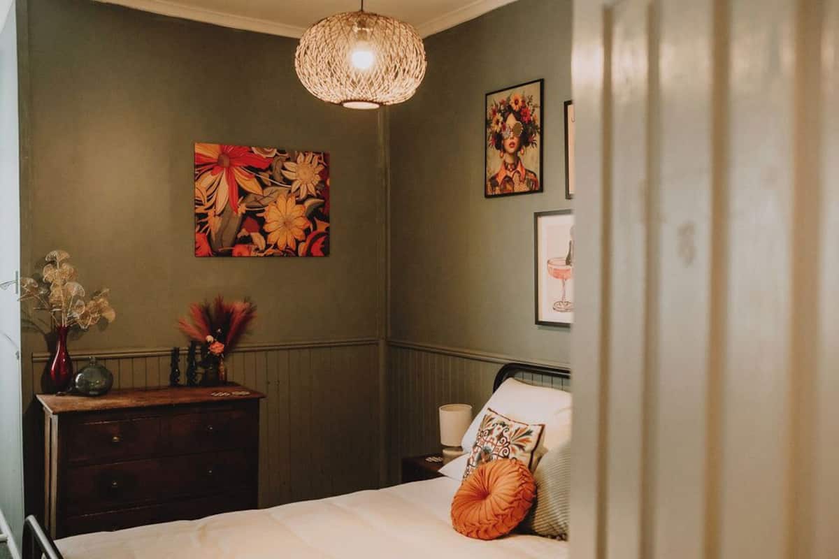 A bedroom with a bed, a dresser, a vase with dried flowers, and two wall-mounted paintings.