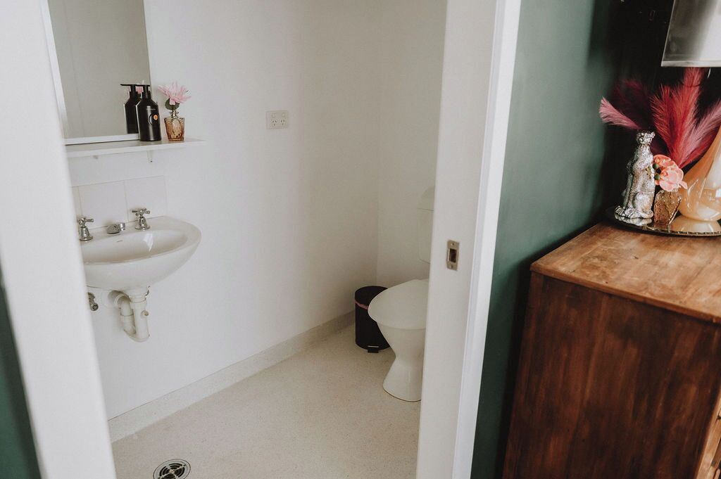 A bathroom with a white sink, mirror, and toilet. There is a wooden cabinet with decorative items on top.