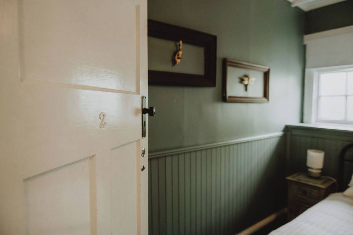 A room with a bed, a nightstand with a lamp, a framed picture on the wall, and a door.