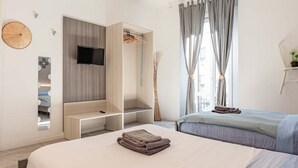 Ein modernes Schlafzimmer mit Bett, einem an einer Holzplatte montierten Fernseher, einem Kleiderschrank mit Kleiderstange und einem Vorhangfenster.