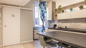 Eine moderne Küche mit dunkler Arbeitsplatte, zwei Barhocker und einem Fenster mit Vorhang.