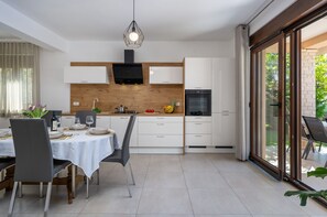 Une cuisine moderne avec des meubles blancs, un mur d’accent en bois et un coin repas avec une table dressée pour deux personnes.