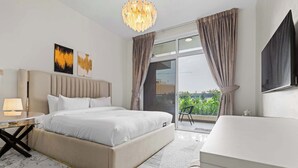 Ett modernt hotellrum med en stor säng, ett sängbord med en lampa, en platt-TV och en balkong med gardiner.