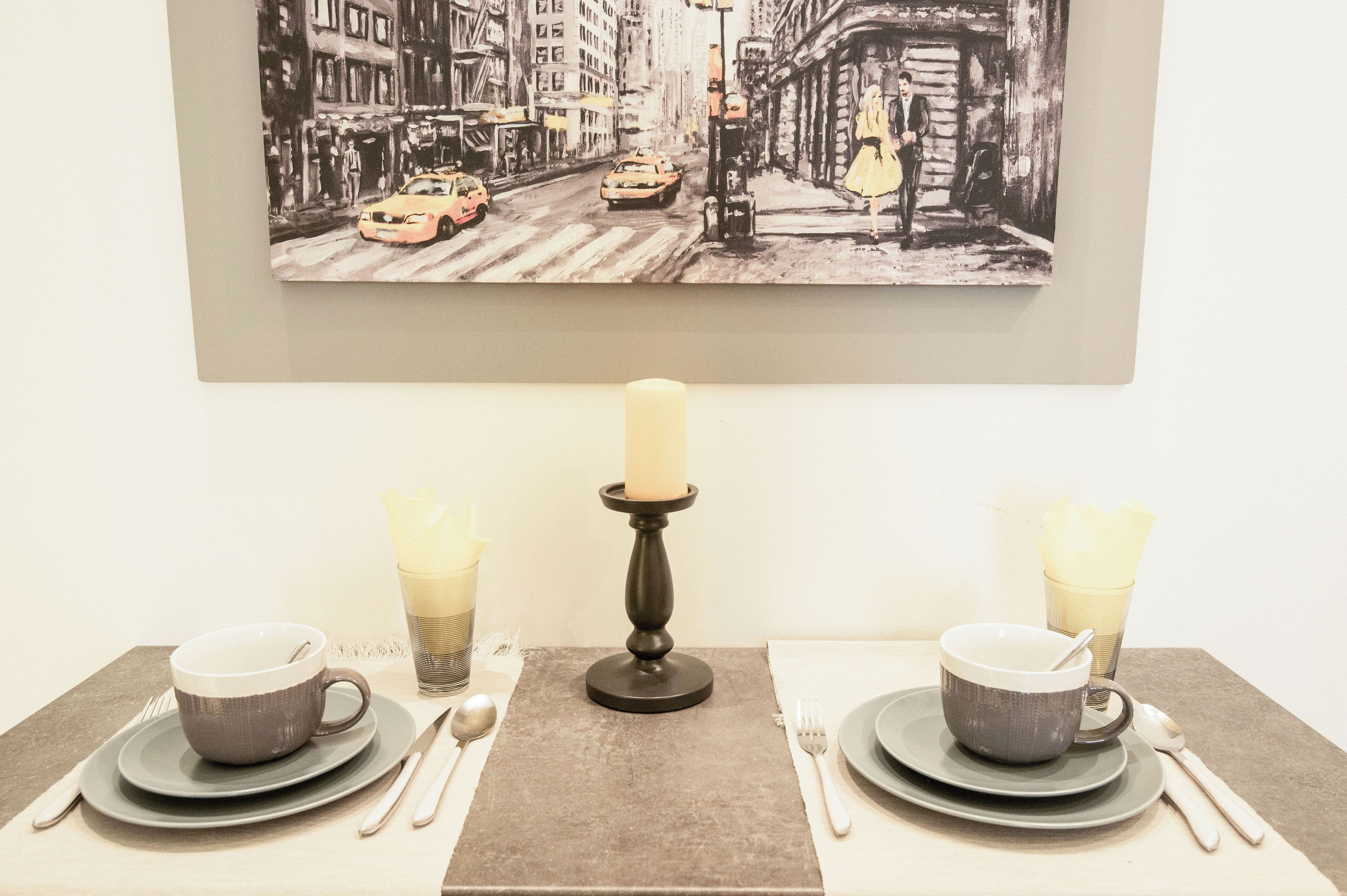 Una mesa de comedor dispuesta con dos tazas, una vela y cubiertos.