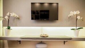Ein moderner Empfangsbereich mit Wand-Fernseher, einer Rezeption mit kleiner Pflanze und je einer Topf-Orchidee auf beiden Seiten.