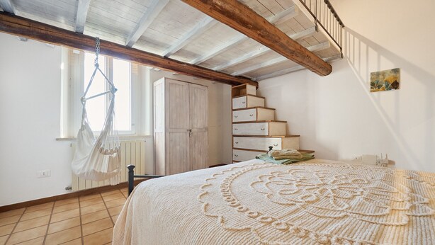 Una camera da letto con un letto, una sedia a dondolo, un armadio, una scala e un quadro appeso al muro.