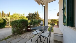 Una terrazza esterna con tavolo e sedie, una lampada e vista sul giardino e le colline circostanti.