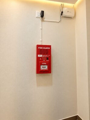 A fire alarm mounted on a wall with a power outlet and a network device above it. - Shree Hari Kunj (Varanasi)