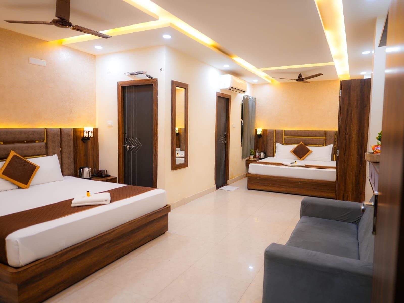 A hotel room with two beds, a sofa, a ceiling fan, and recessed lighting.