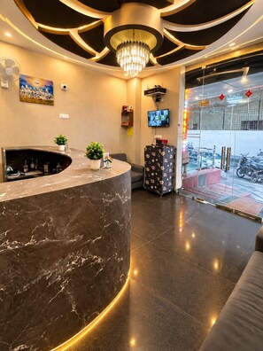 A reception area with a marble counter, a chandelier, a television, and a view of the parking area. - Shree Hari Kunj (Varanasi)