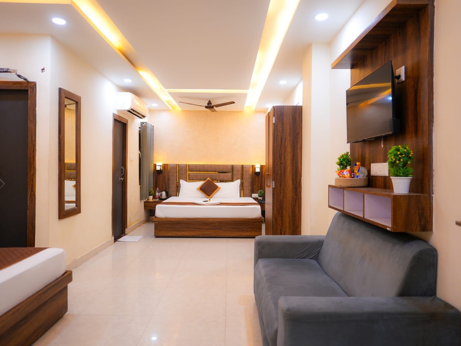 Habitación de hotel moderna con una cama grande, un televisor de pantalla plana, un ventilador de techo y una zona de estar con sofá.