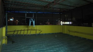 Ruime, open binnenruimte met een hoge plafond en metalen balken. Een gele muur en een raam met uitzicht op de stad 's nachts.