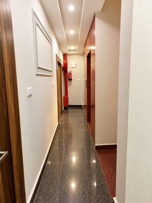 A hallway with a polished floor, a fire extinguisher mounted on the wall, and a door on the left. - Shree Hari Kunj (Varanasi)