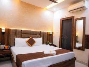 Une chambre d’hôtel avec un grand lit, une tête de lit en bois, des tables de chevet, un appareil de climatisation, un miroir et une porte ornée d’un motif géométrique.