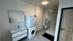 A modern bathroom with a built-in washing machine, a sink, and a glass shower enclosure. - Au 8 Duplexe du coin (Flémalle)