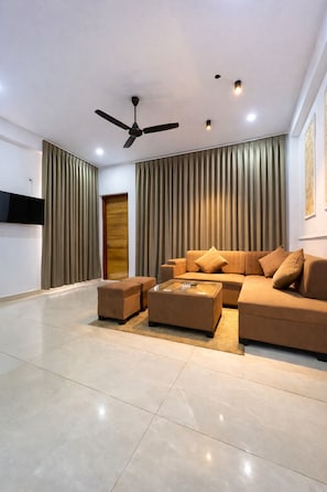 A modern living room with a sectional sofa, a coffee table, a ceiling fan, and a flat-screen TV mounted on the wall.